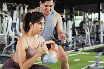 Portrait of Asian women in sportswear doing squats workout in fitness gym with her handsome muscular personal trainer. Concept Exercise for good shape