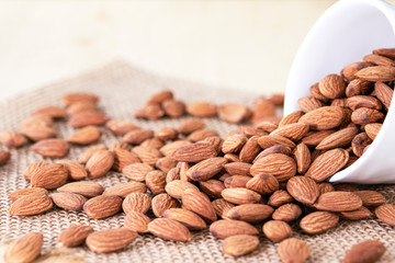 Closeup of almonds nut in white bowl were poured on sacks. Almond nut is popular and high protein nutrition.