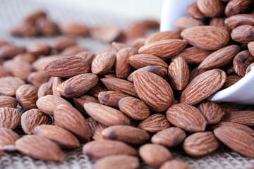Closeup of almonds nut in white bowl were poured on sacks. Almond nut is popular and high protein nutrition.