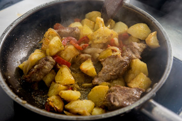 Chef cooks fried potatoes with pieces of meat in a restaurant kitchen