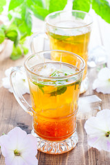 Black iced tea with lemon and mint in glass cups on a wooden table, selective focus