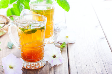 Black iced tea with lemon and mint in glass cups on a wooden table, horizontal, copy space