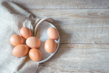 Brown eggs on a plate with textile napkin on wooden rustic background. Easter composition, mockup. 