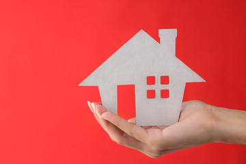 Home purchase concept. Small decorative white house in a hand on a red background