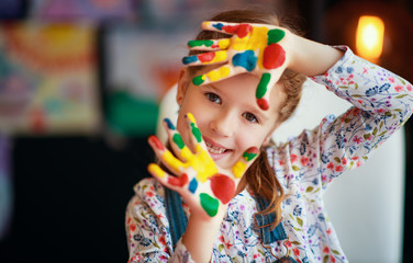 funny child girl draws laughing shows hands dirty with paint.