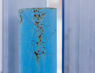 A rusty metal pipe, Rust through the blue paint on an iron post.