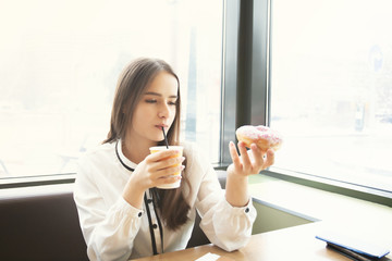 Young woman has breakfast in a cafe, eats a donut, drinks coffee