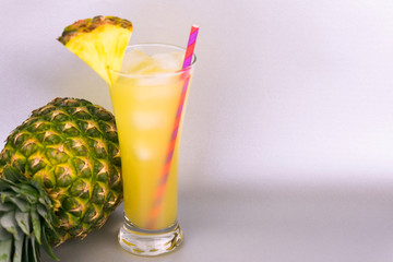  Pineapple juice in a tall glass and pineapple on a gray background. Copy space.