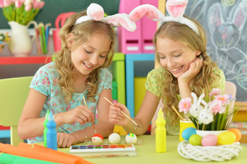 Obraz na płótnie Canvas Girls wearing rabbit ears decorating Easter eggs at home
