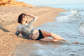 Fototapeta na wymiar A young girl is sunbathing on a beach made of pebbles, taking sun and sea baths.