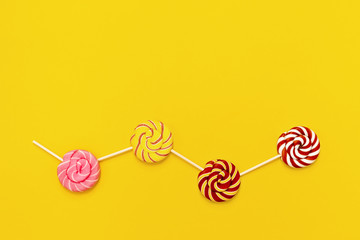 Sweet round candy lollypops with stripes on stick on yellow paper background with copy space. Creative concept still life sweets for Birthday, party, holidays. Top view and flat lay.