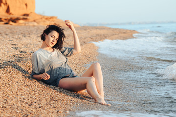 Fototapeta na wymiar A young girl is sunbathing on a beach made of pebbles, taking sun and sea baths.