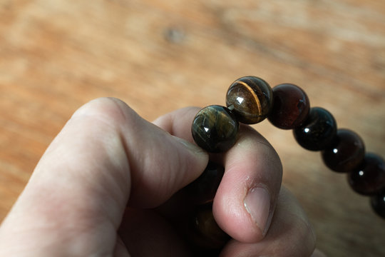 Woman's left hand praying and counting brown beads rosary in blurred wood  background, Close up and macro shot, Select focus, Asian Body language feeling, Prayer buddhist, Religious concept