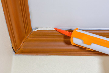 Technician man hand using glue gun or manual caulking gun with polyurethane silicone to repair and fix the wooden cornice with the ceiling. Installation or renovation interior concept.  © NIKCOA