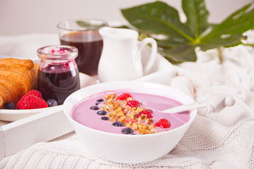 Smoothie bowl with berries. Croissant bun, glass of coffee, jar of milk, jam nearby.