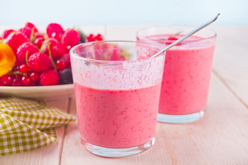Two glasses of berries smoothie and plate with berries.