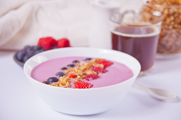 Smoothie bowl with berries. Croissant bun, glass of coffee, jar of milk, jam nearby.