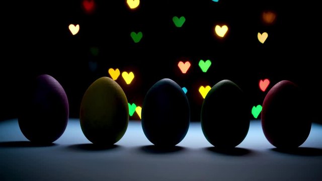 Happy easter concept. Searchlight illuminates bright colored eggs standing in a row on black background with colorful heart shaped lights.