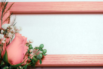 A peachy orange rose flower bud with white baby's breath (Gypsophila) and green hypericum berries against a peachy-orange wood frame and off-white background, with copy space
