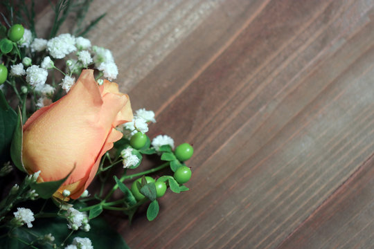A peachy orange rose flower bud with white baby's breath (Gypsophila) and green hypericum berries against a dark brown wood background, with copy space