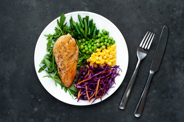 salad of chicken breast, arugula, red cabbage, carrots, corn, green peas, green beans in a white plate on a stone background