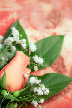 A peachy orange rose flower bud with white baby's breath (Gypsophila) and green hypericum berries against a soft background of eco-printed silk, with copy space