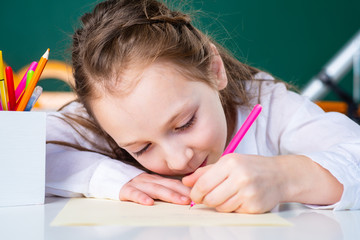 Child girl drawing picture in class. Close up face.