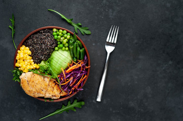 Bowl Buddha.Quinoa, chicken breast, avocado, red cabbage, arugula, carrot, green  peas, corn, broccoli, green beans in a plate on a stone background, with copy space for your text