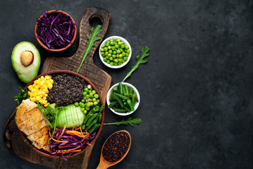 Bowl Buddha.Quinoa, chicken breast, avocado, red cabbage, arugula, carrot, green  peas, corn, broccoli, green beans in a plate on a stone background, with copy space for your text