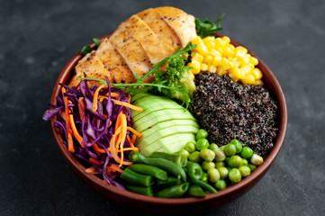 Bowl Buddha.Quinoa, chicken breast, avocado, red cabbage, arugula, carrot, green  peas, corn, broccoli, green beans in a plate on a stone background.