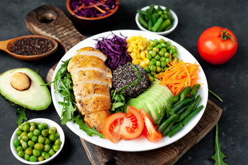 Bowl Buddha . Quinoa, chicken breast, arugula, avocado, red cabbage, carrot, green  peas, corn, tomato, green beans in a white plate on a stone background.