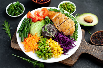 Bowl Buddha . Quinoa, chicken breast, arugula, avocado, red cabbage, carrot, green  peas, corn, tomato, green beans in a white plate on a stone background.