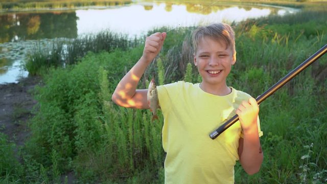 Closeup 4k video portrait of cute happy smiling kid proud himself to catch his first fish in lake in countryside during summer holidays.