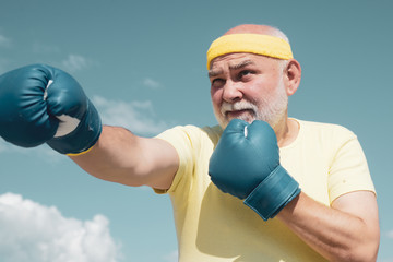 Handsome elderly man practicing boxing kicks. Elderly man hitting punching bag. Senior men fighting poses. Senior sport man wearing boxing gloves.