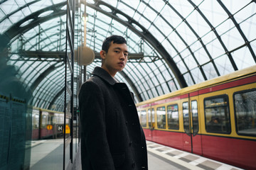 Young stylish Asian businessman in coat confidently looking in camera at subway station