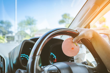 Hungry woman driving her car while eating bologna with ice coffee in the traffic. Selective focus on bologna. © JinnaritT