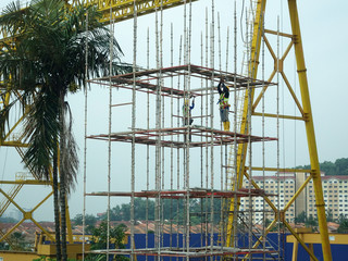 KUALA LUMPUR, MALAYSIA -JULY 28, 2019: Construction workers wearing safety gear and safety harness while installing scaffolding at a high level in the construction site.