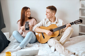 Obraz na płótnie Canvas cheerful happy couple spending great time in the bedroom, close up photo. man and woman sitting on the bed and using camera nd guitar