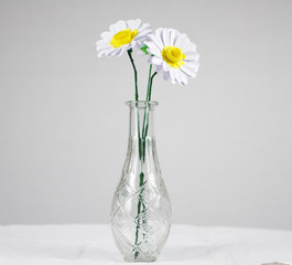 zwei gebastelte gerbera blüten aus pappe  karton mit gelb weisser blüte grünen stielen in glasvase vor weißem hintergrund margarite