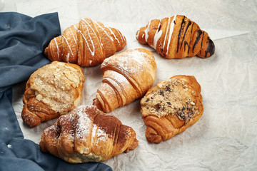 Freshly baked croissants with different fillings on parchment. Appetizing French pastries for breakfast. Different assortment, lots of croissants