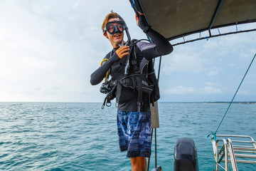 young diver in a suit and diving equipment is preparing to jump from boat into the water