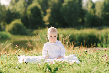 A small child sits on a blanket on the shore of the lake in the open air. Summer walks with your baby