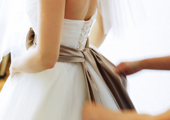 Morning of the bride. A friend ties a bow on the bride's dress. Selective focus