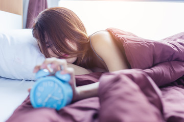 Obraz na płótnie Canvas Wake up asleep young asian woman stopping alarm clock on cozy bed in morning. Portrait young sleeping asian girl and alarm clock in bedroom at home. Working woman turning off alarm clock, lazy wakeup