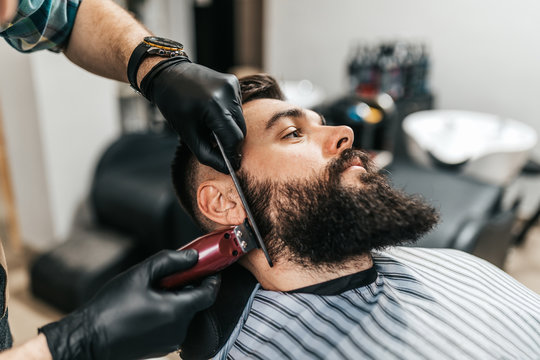 Young good looking man visiting barber shop. Trendy and stylish beard styling and cut.