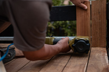 Hand man carpenter using air nail gun to complete wood table in garden