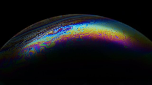 Multicolored rainbow iris of soap bubble. Fantastic colorful planet on black background. Abstract multi-colored surface overflows
