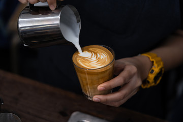 Close-up of barista hand holding and pouring hot milk for prepare latte art on piccolo latte cup of coffee. - obrazy, fototapety, plakaty