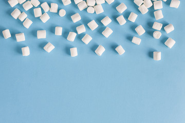 Frame of white marshmallows on a blue background. Flatlay or top view. Background of white mini marshmallows. Concept of snow, winter mood, food.