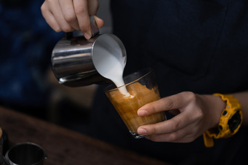 Close-up of barista hand holding and pouring hot milk for prepare latte art on piccolo latte cup of coffee.